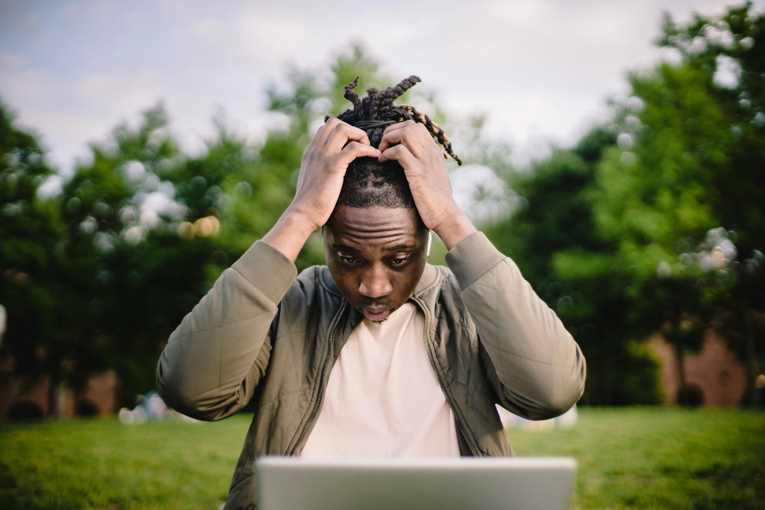 top business mistakes Upset young African American male freelancer clutching head with hands after failure in project while working remotely in park