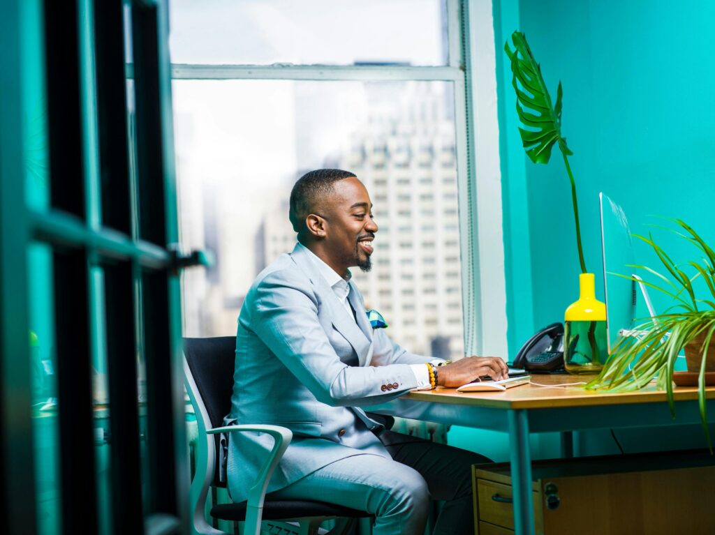 Confident businessman in modern office working on laptop with city view. Essential Skills Every Digital Marketing Strategist Needs in 2025