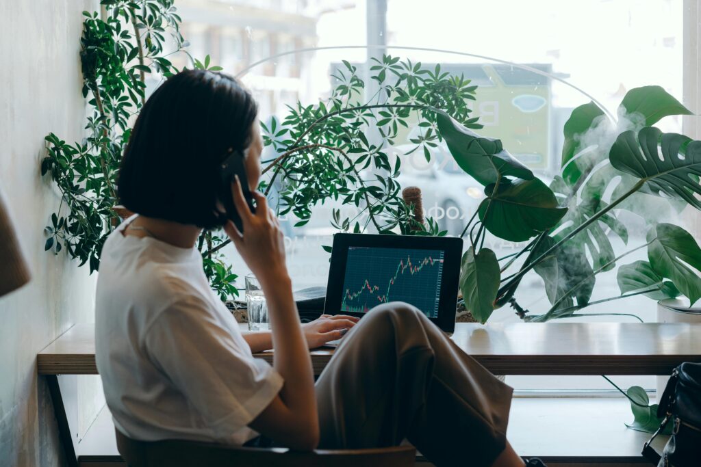 Businesswoman on phone, analyzing marketing graphs on laptop in a café. What Is the Marketing Environment? Guide for Marketers and Business Leaders